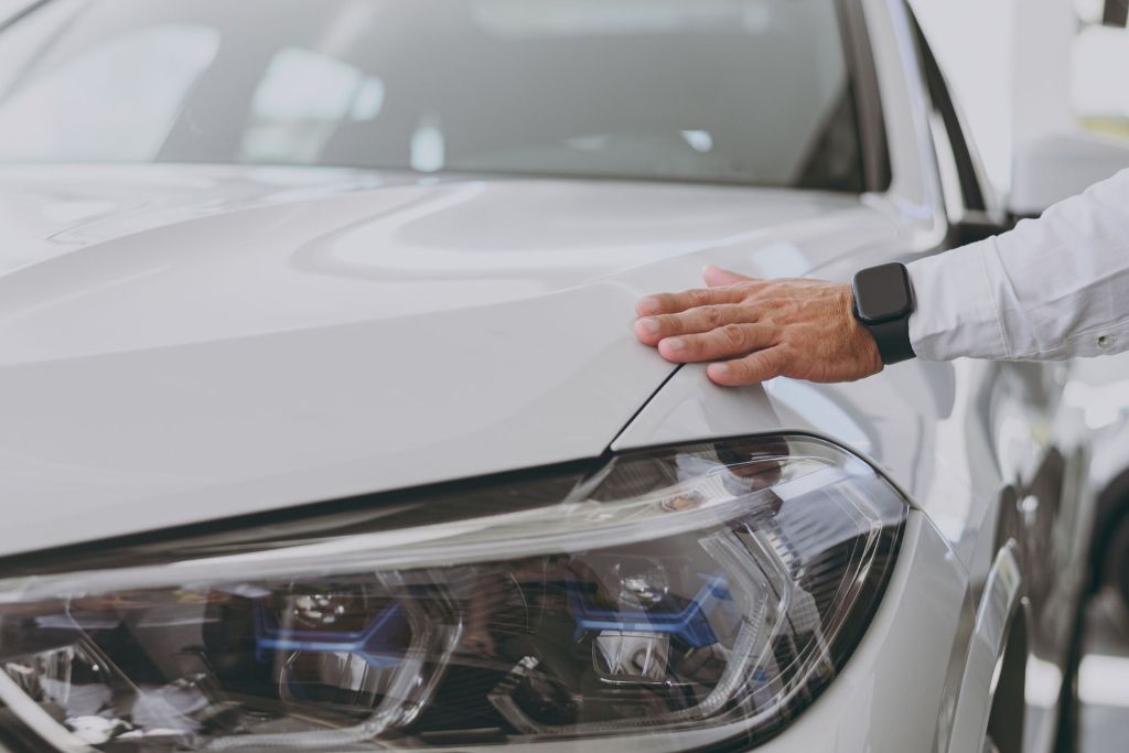 Demonstration of mechanophilia were man's hand in white sleeve shirt touching front fender of a beauitiful white sport car.
