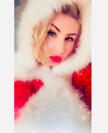 Goddess Jazzy in a Santa-style dress with a white fur hood over the head and red lipstick