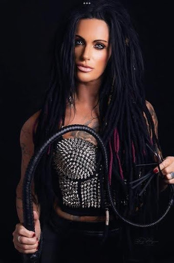 Mistress Raven in silver spike cover top holding a black leather long flexible whip