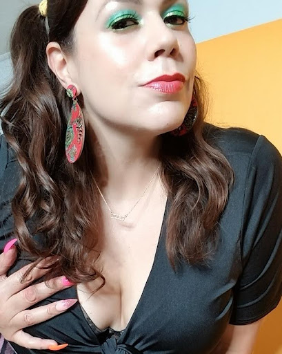 Queen Mixtrix with colorful makeup, green shades over eyes, red lipstick, posing in a dark green blouse with a cut to expose her huge of bubs