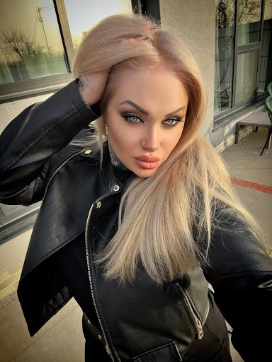 Mistress Goldy posing with her fluffy lips and black leather jacket for selfie on a busy street outdoor