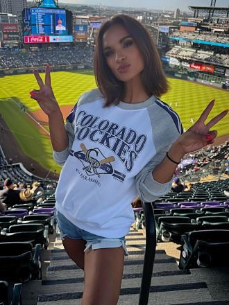 Ashley Sinclair standing on a grandstand and posing against a background of a crowded baseball arena