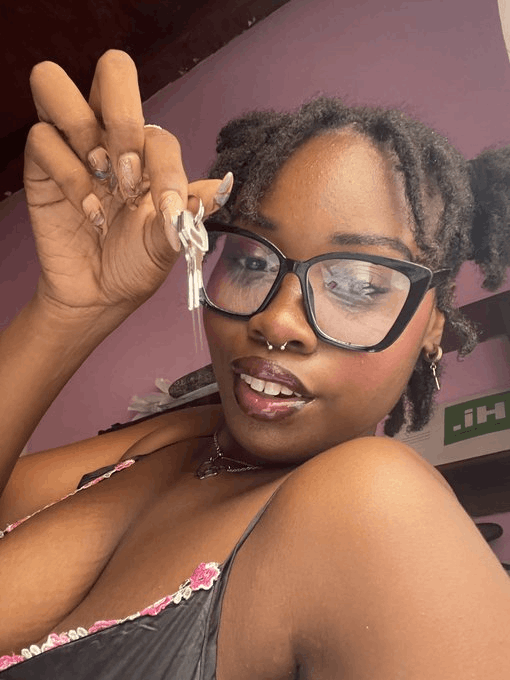 Eliteress Elaine, in a black bra and black-framed glasses, shows keys from the chastity cage of her sub